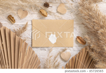 Blank envelope on white wooden table near dried plants, palm leaves, pampas grass and hearts Blank envelope on white wooden table near dried plants, palm leaves, pampas grass and hearts 85726565