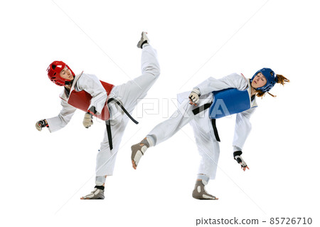 Dynamic portrait of two young women, taekwondo athletes training together isolated over white background. Concept of sport, skills 85726710