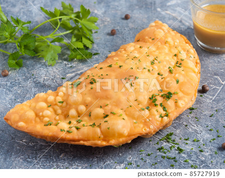 cheburek with meat and mustard dressing, decorated with greens on a gray background cheburek with meat and mustard dressing, decorated with greens on a gray background 85727919
