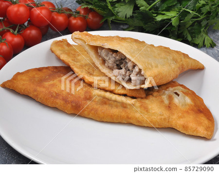 cheburek with beef and pork on a white plate decorated with vegetables and herbs cheburek with beef and pork on a white plate decorated with vegetables and herbs 85729090