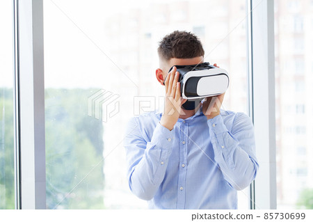 Attractive bearded man enjoyingvirtual reality glasses in modern interior design coworking studio. 85730699