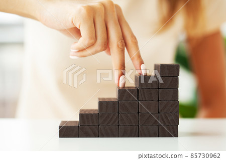 Hand putting wood cube on top of wood block stacking as step stair Hand putting wood cube on top of wood block stacking as step stair 85730962