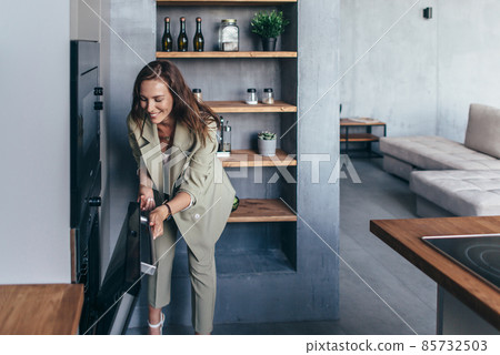 Woman peeks into the oven to check on a baked dish Woman peeks into the oven to check on a baked dish 85732503