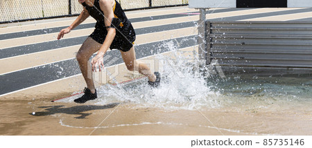 Runner running out of the water of a steeplchase pit during a race Runner running out of the water of a steeplchase pit during a race 85735146