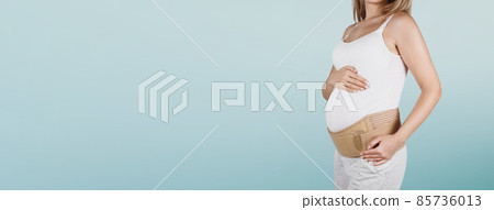 Pregnant woman belly in prenatal pregnancy maternity belt isolated on blue background. Orthopedic abdominal support waist, back, abdomen band. Belly Brace for pregnancy. Horizontal banner or poster. 85736013