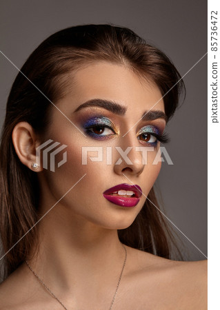 Naked female in necklace and earrings posing on gray background. Bright makeup, perfect skin. Colorful eyeshadow, long eyelashes, red lips. Close up Naked female in necklace and earrings posing on gray background. Bright makeup, perfect skin. Colorful eyeshadow, long eyelashes, red lips. Close up 85736472