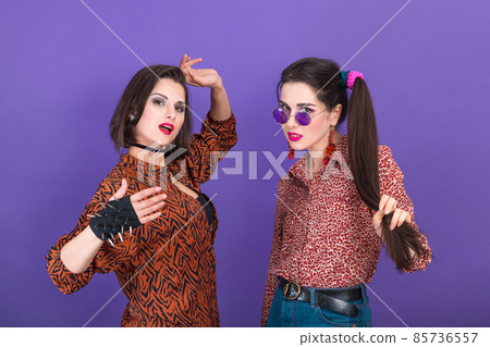 Two cute young women dressed in 80s style fooling around on violet background 85736557