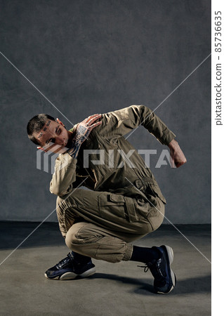 Extraordinary man with tattooed body, earrings, beard. Dressed in khaki overalls and black sneakers. Dancing on gray background. Dancehall, hip-hop Extraordinary man with tattooed body, earrings, beard. Dressed in khaki overalls and black sneakers. Dancing on gray background. Dancehall, hip-hop 85736635