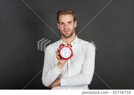 Serious guy holding alarm clock dark background, time 85736758
