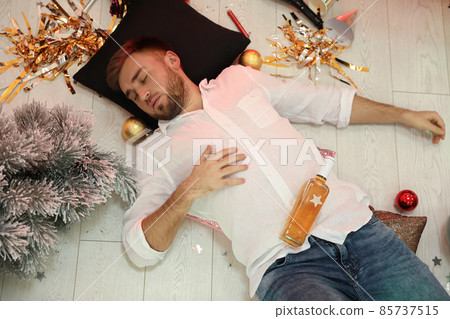 Drunk man sleeping on floor in messy room after New Year party, above view Drunk man sleeping on floor in messy room after New Year party, above view 85737515