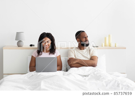 Offended sad young african american man with crossed arms on his chest ignores woman with computer Offended sad young african american man with crossed arms on his chest ignores woman with computer 85737659