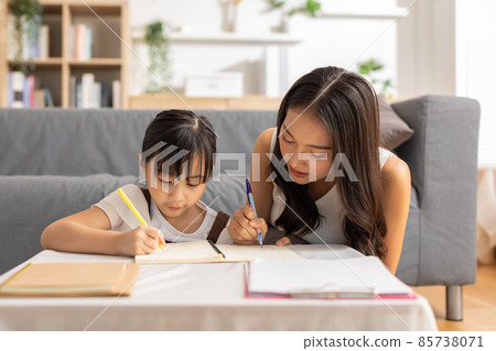 Happy Asian little girl doing homework with mother at home. Asian young mother teaching small daughter to drawing reading and writing to develop her daughter skill. Home School Concept Happy Asian little girl doing homework with mother at home. Asian young mother teaching small daughter to drawing reading and writing to develop her daughter skill. Home School Concept 85738071