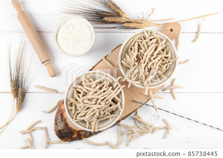Whole grain wheat raw apulian pasta called Pizzarieddi or maccaruni on a ceramic plate on white wooden table 85738445