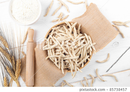 Whole grain wheat raw apulian pasta called Pizzarieddi or maccaruni in a sieve on white wooden table 85738457