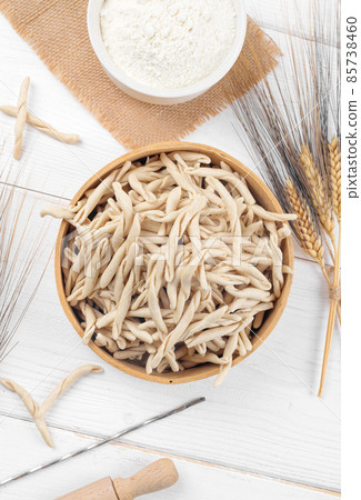 Whole grain wheat raw apulian pasta called Pizzarieddi or maccaruni in a sieve on white wooden table 85738460