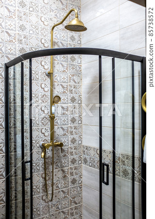 A round brass shower head and a transparent shower cubicle in the 85738572