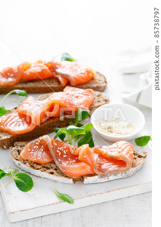 Whole grain rye bread open sandwiches with salted salmon on a white rustic wooden table. Healthy food 85738797