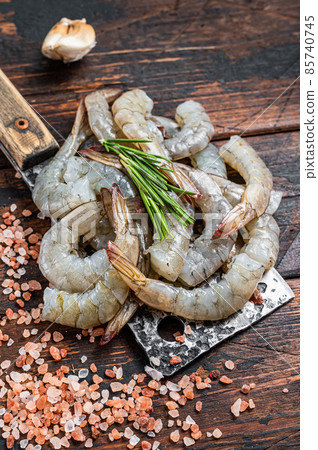 Raw Headless tiger shrimps prawns on a butcher cleaver. Dark wooden background. Top view Raw Headless tiger shrimps prawns on a butcher cleaver. Dark wooden background. Top view 85740745