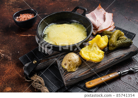 Swiss Raclette Melted cheese with boiled potato and ham on wooden board. Dark background. Top view 85741354