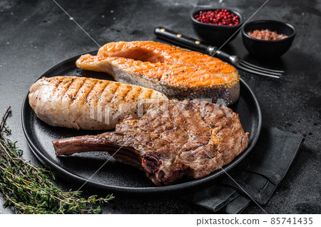 Grilled meat steaks - fish salmon, beef veal and turkey fillet. Black background. Top view Grilled meat steaks - fish salmon, beef veal and turkey fillet. Black background. Top view 85741435