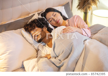 Woman hugging man lying in bed with closed eyes Woman hugging man lying in bed with closed eyes 85742395