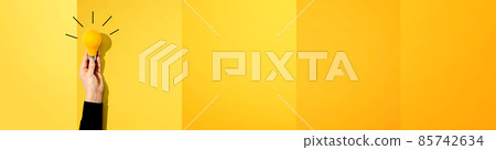 Person holding a yellow light bulb 85742634