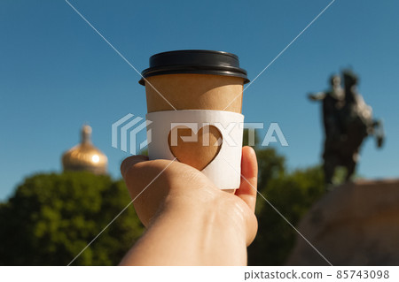 cup of natural coffee with carved white heart in woman's palm on background of Bronze Horseman in St. Petersburg, Russia 85743098
