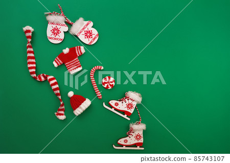 decorative knitted ornaments scarf, sweater, hat and caramel, wooden decorative mittens and skates in red and white color on green background 85743107