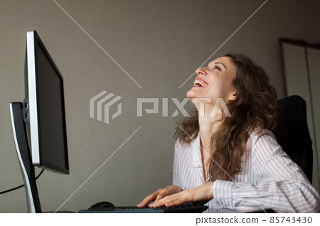 Young female office manager in white shirt and curly hair is sitting at the table and typing using keyboard, routine work, freelance Young female office manager in white shirt and curly hair is sitting at the table and typing using keyboard, routine work, freelance 85743430