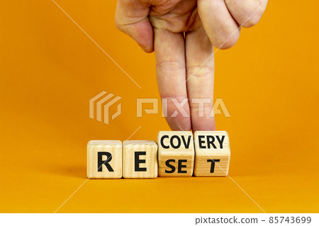 Recovery and reset symbol. Businessman turns cubes and changes the word 'recovery' to 'reset'. Beautiful orange background. Business and recovery - reset concept. Copy space. Recovery and reset symbol. Businessman turns cubes and changes the word 'recovery' to 'reset'. Beautiful orange background. Business and recovery - reset concept. Copy space. 85743699