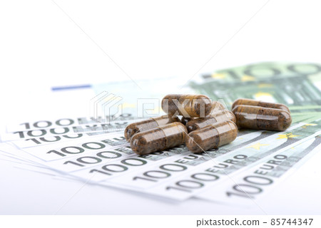 Close-up of a group of dietary supplements or vitamins tablets on defocused one hundred euro banknotes. Close-up of a group of dietary supplements or vitamins tablets on defocused one hundred euro banknotes. 85744347