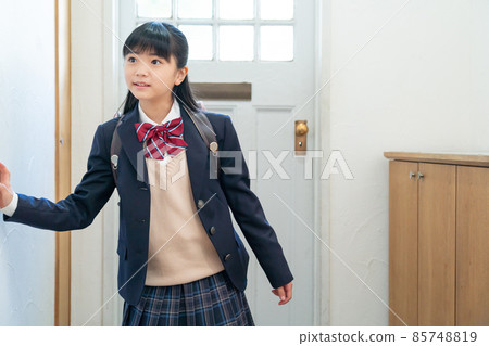 Girl in school uniform standing at the front door 85748819