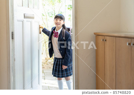 Girl in school uniform standing at the front door 85748820