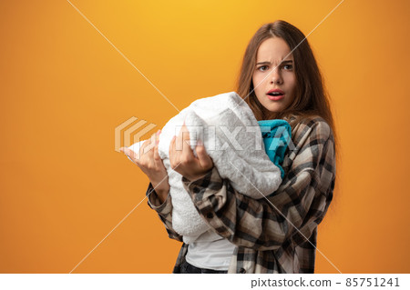 Teen girl holding dirty laundry against yellow background 85751241