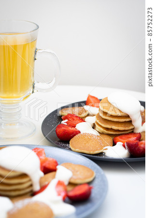Mini pancakes with sour cream sauce and strawberries on plates, breakfast for the family. Front view. 85752273