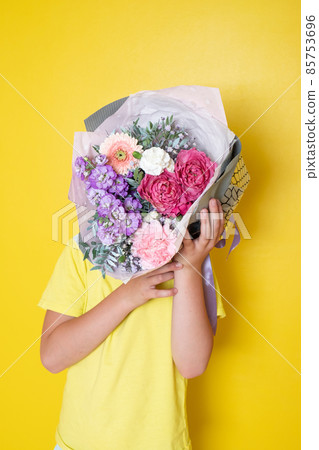 The boy holds a flower arrangement in a round box. A gift for Mom The boy holds a flower arrangement in a round box. A gift for Mom 85753696