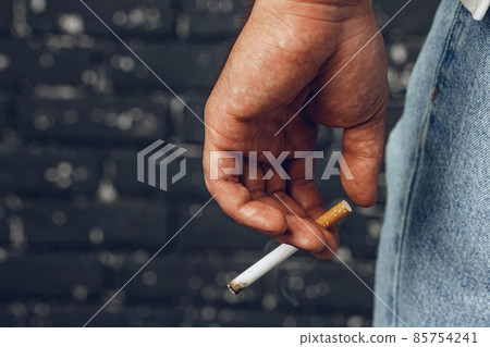 Male hand holding lit cigarette against black background 85754241