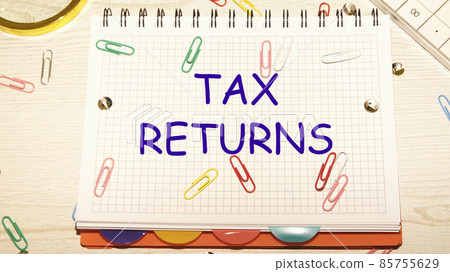 tax return text on a notebook in a cage with scattered paper clips on a notebook and a table tax return text on a notebook in a cage with scattered paper clips on a notebook and a table 85755629