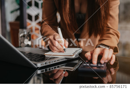 Businessman hand working at a computer and writing on a notepad with a pen in the office on the desk there a calculator. Businessman hand working at a computer and writing on a notepad with a pen in the office on the desk there a calculator. 85756171