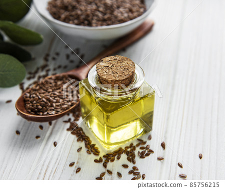 Flax seeds or linseeds in spoon and bowl with glass of linseed oil 85756215