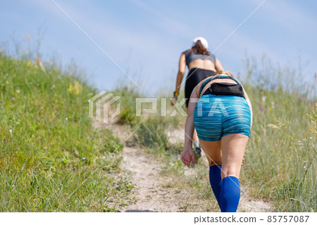 Tired sportswomen ascending hill on trail running contest Tired sportswomen ascending hill on trail running contest 85757087
