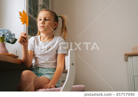 Low-angle view of little girl holding beautiful dried maple leaf to create herbarium diy at home. Low-angle view of little girl holding beautiful dried maple leaf to create herbarium diy at home. 85757090