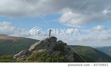 Happy man at top of mountain celebrates climb to peak by jumping, dancing. Backdrop of mountains, blue sky, clouds. Caucasian man rejoices at achieved success in mountains. Success, victorious concept 85759931