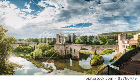 Besalu, Girona, Catalonia, Spain. Famous Landmark Old Medieval Romanesque Besalu Bridge Over The Fluvia River In Cloudy Summer Day 85760479
