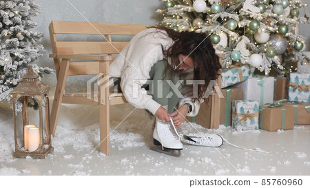 Young pretty woman wearing mittens lacing ice skates before skating Young pretty woman wearing mittens lacing ice skates before skating 85760960