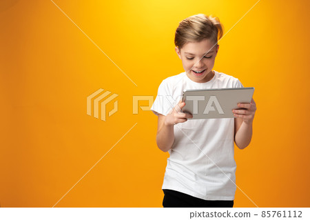 Little boy playing with digital tablet against yellow background 85761112