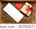 Wooden box with present wrapped in brown craft paper with red ribbon, with empty blank card 85762672