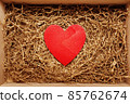 Present box with big red heart lying on brown shredded craft paper filler 85762674