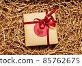 Present box wrapped in brown craft paper with red ribbon, filled with paper filler 85762675