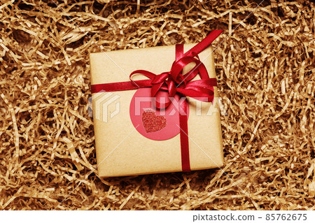 Present box wrapped in brown craft paper with red ribbon, filled with paper filler Present box wrapped in brown craft paper with red ribbon, filled with paper filler 85762675